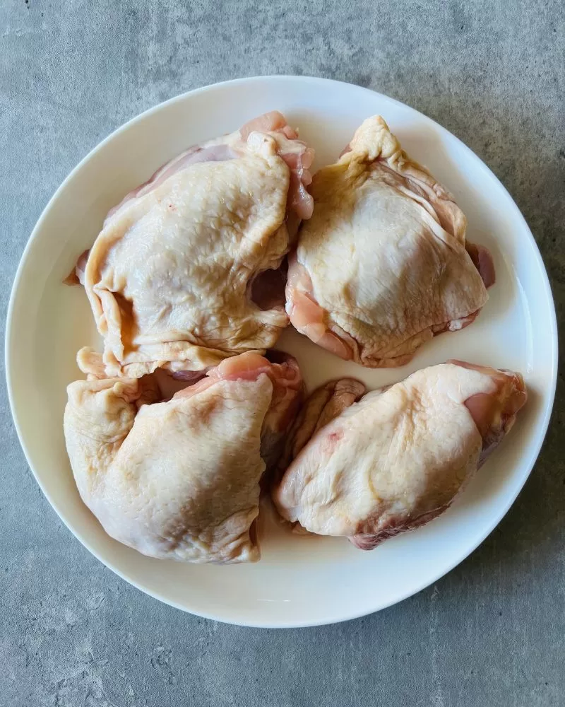 raw chicken thigh cutlets on white plate. grey background