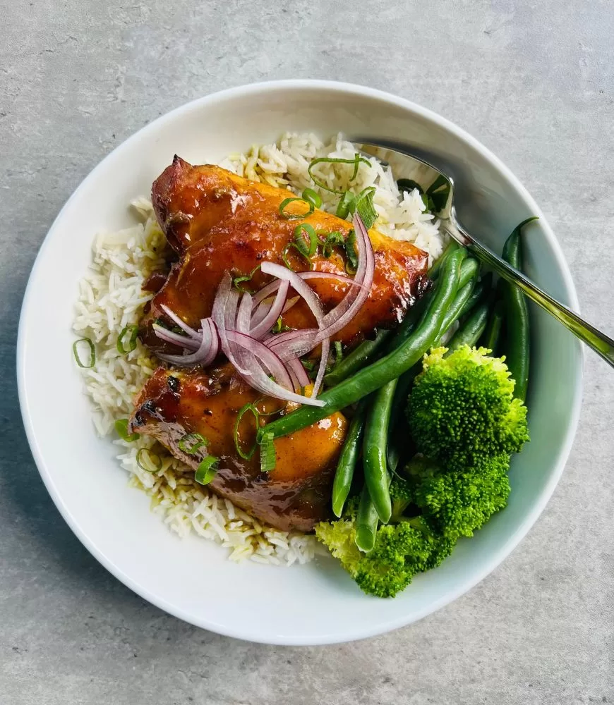 5 ingredient sticky curried honey chicken in white bowl, grey background, silver fork