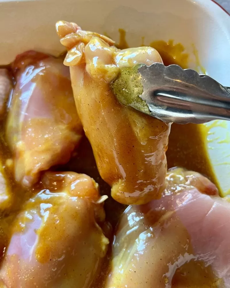 turning raw chicken in baking dish for curried honey chicken