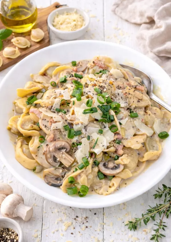 Bowl of creamy French onion tortellini with crispy bacon, sautéed mushrooms, and spring onions, ready to serve.