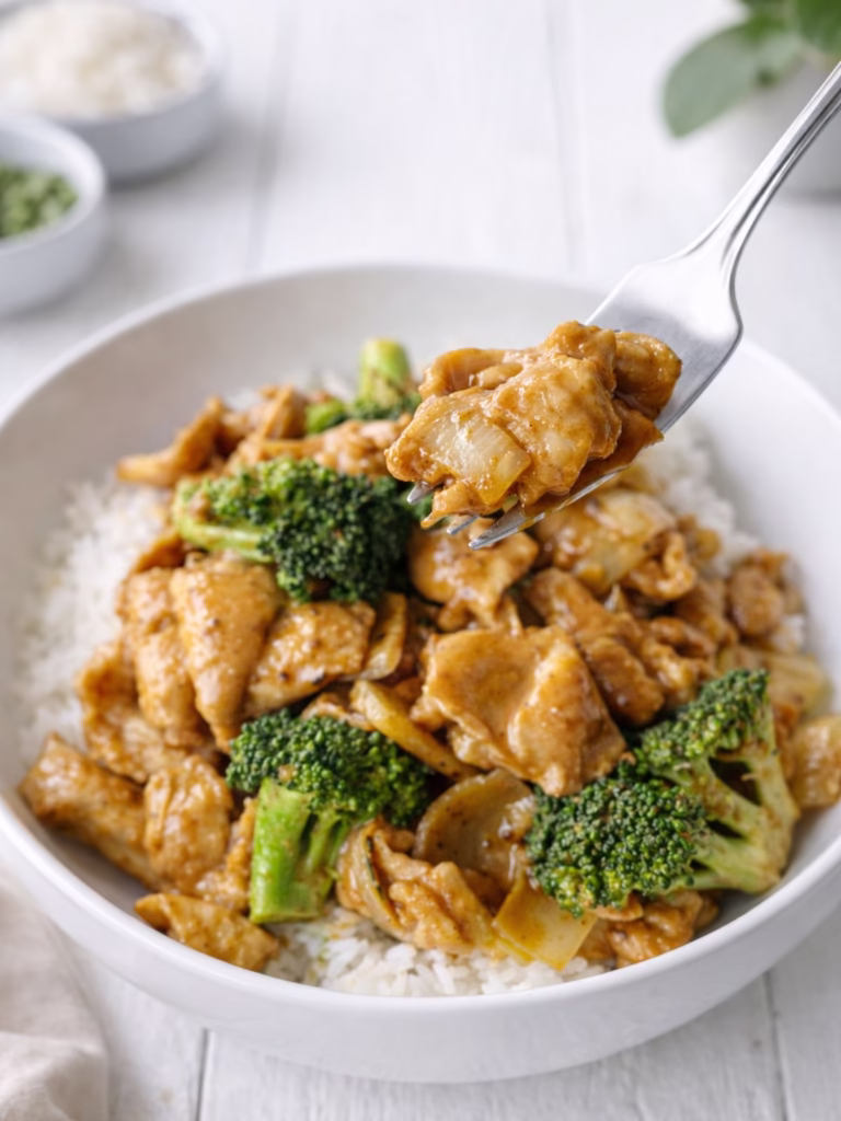 Fork lifting satay chicken with Jimmy’s saté sauce over rice with broccoli and onion