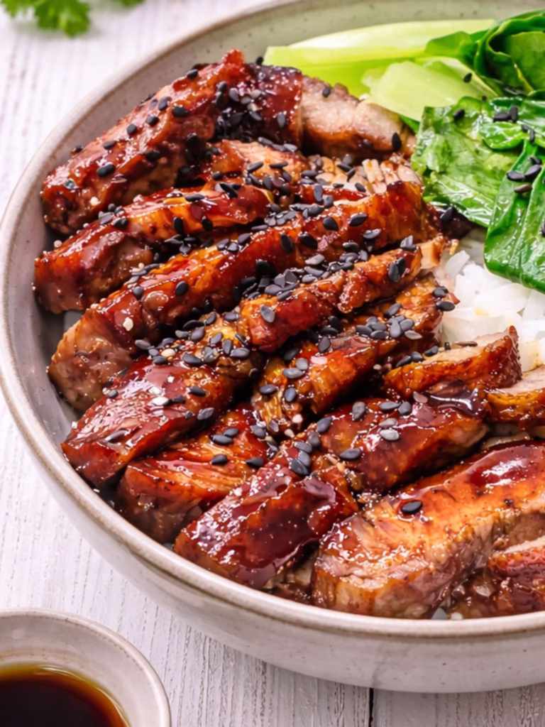 Close up of Char siu BBQ pork sliced over white rice with steamed bok choy, black sesame seeds,