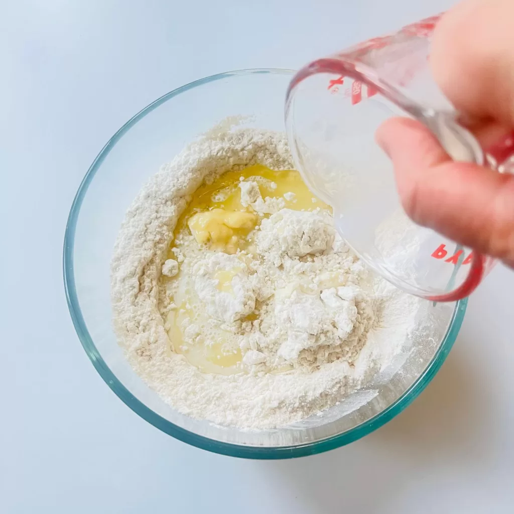 Milk being poured into a bowl of flour with oil already added in the centre of the well.
