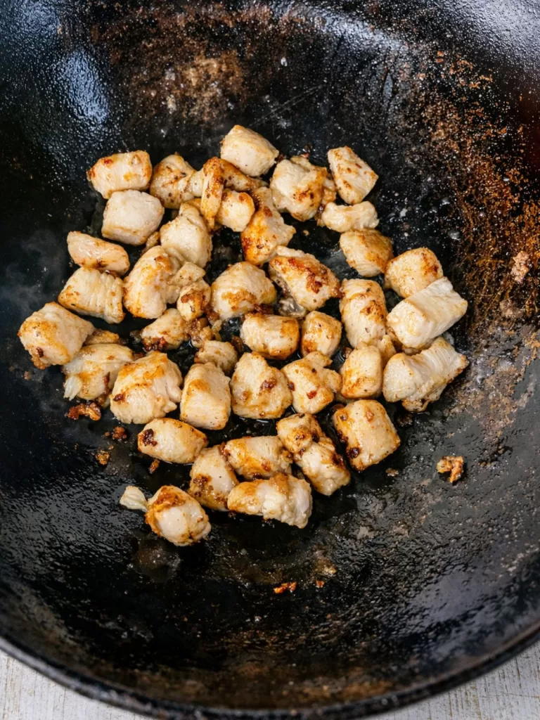 stir-frying chicken pieces in a seasoned wok.