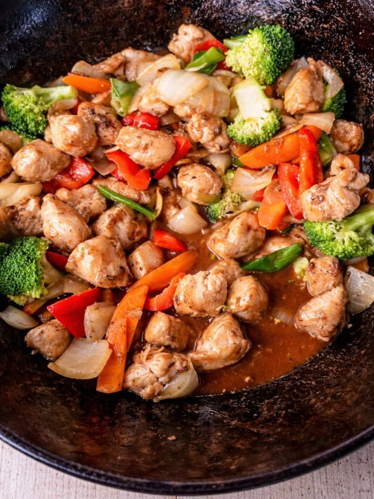 Chinese chicken stir-fry in a wok with broccoli, carrots, red capsicum and onions in a glossy savoury sauce.