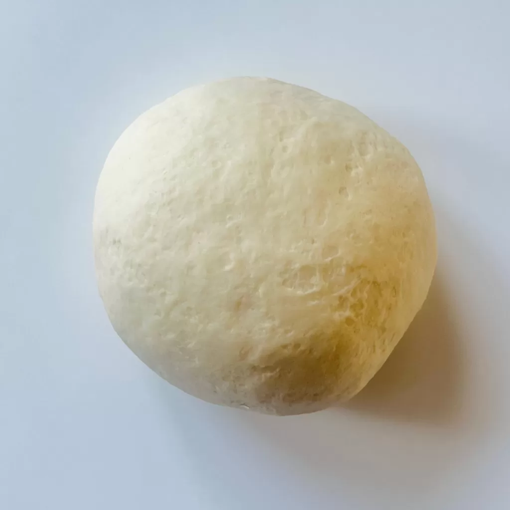 A smooth, soft flatbread dough ball resting on a white surface after kneading.