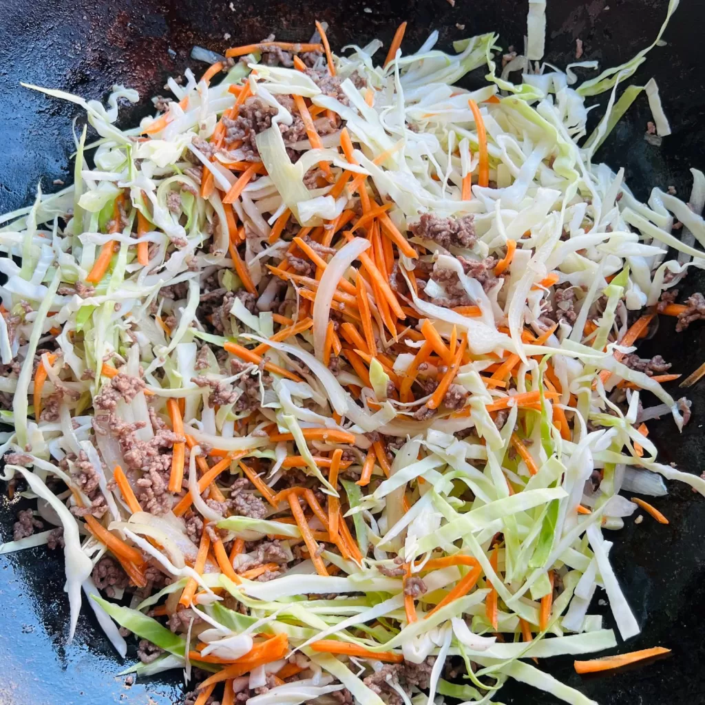 Shredded cabbage and carrot added to beef mince in a wok