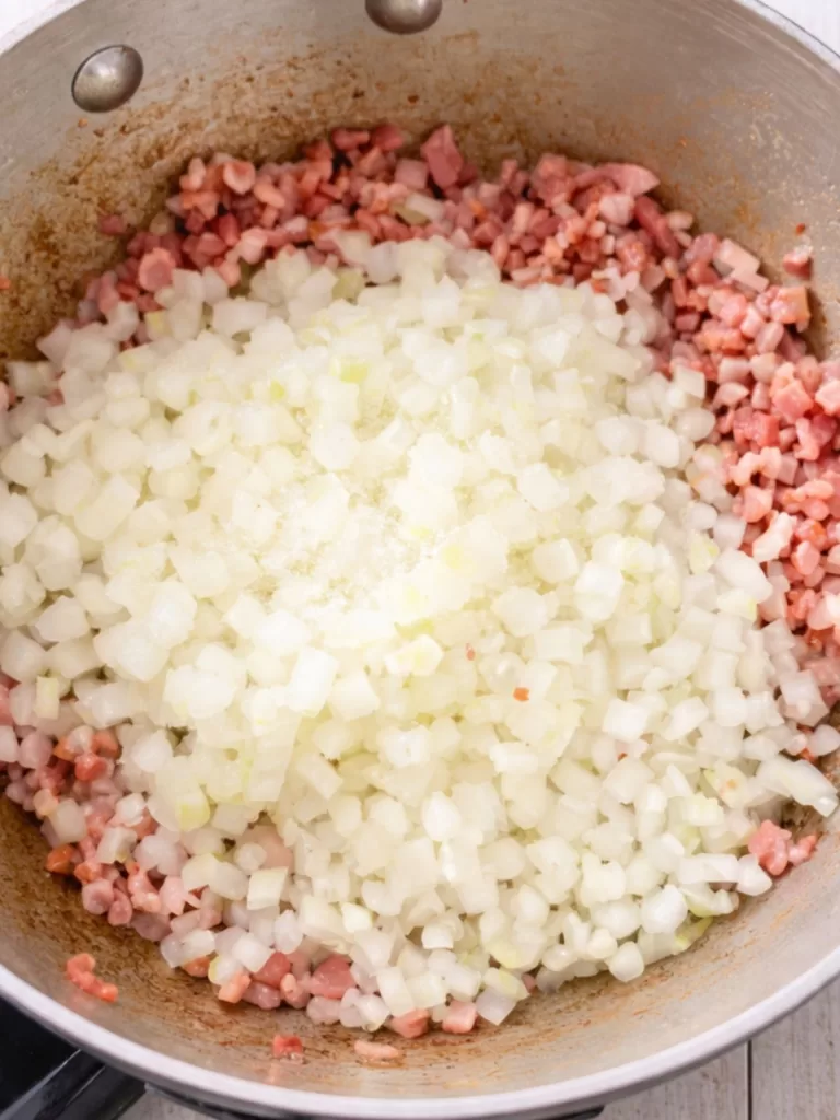 Diced onion and bacon cooking together in a saucepan on a white timber surface, photographed from above in natural light.