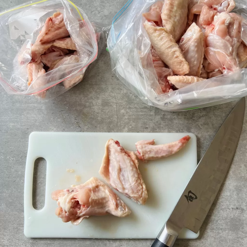 Chicken wings cut into wingettes on a chopping board with a knife