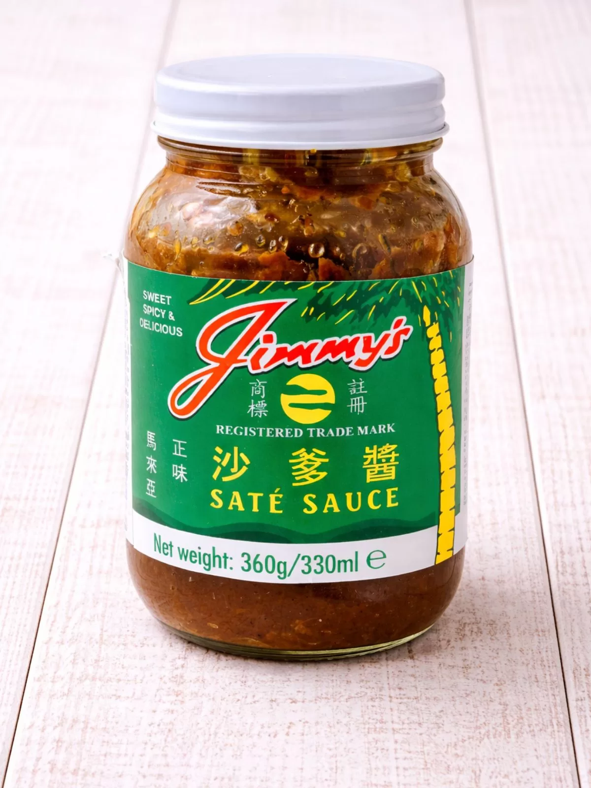 Glass jar of sate sauce on white timber background.