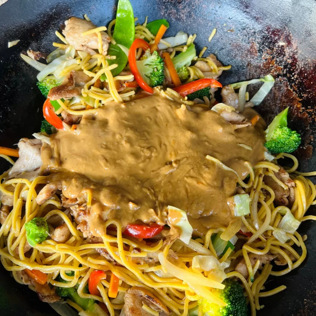 Satay sauce poured over the noodles, chicken and vegetables in the wok.