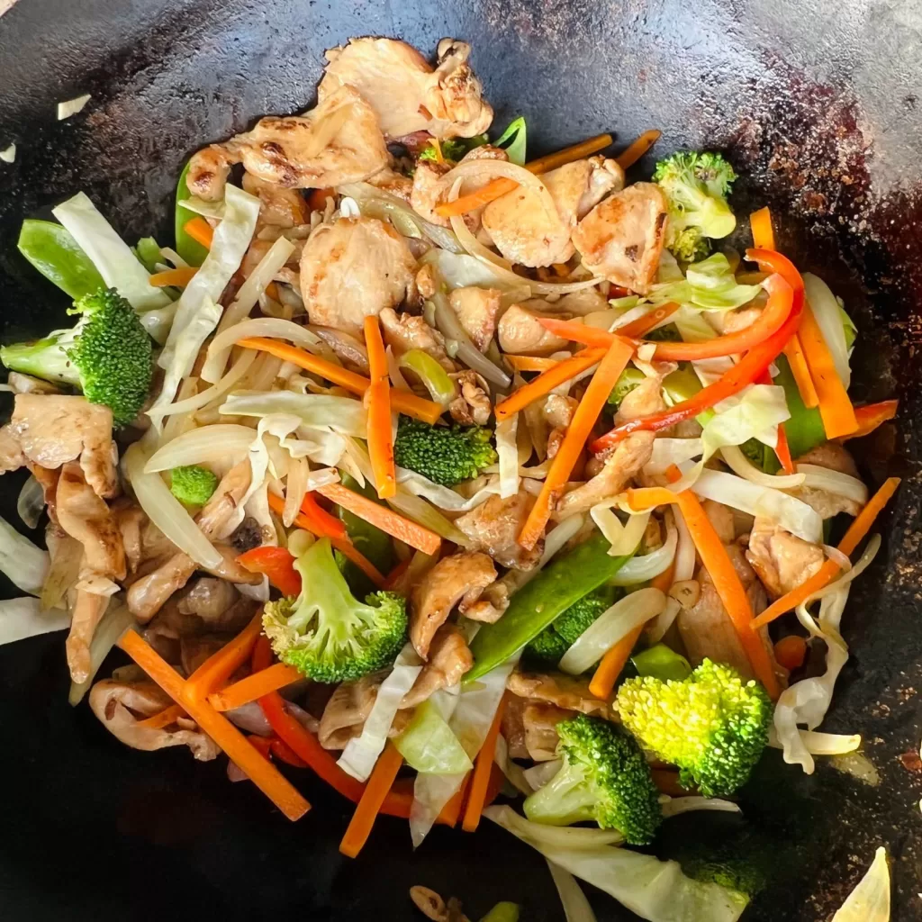 Stir-fried chicken mixed with vegetables in a wok for satay chicken noodles.