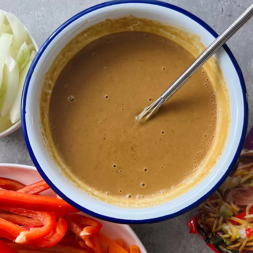 Bowl of satay sauce with sliced vegetables prepared for satay chicken noodles.