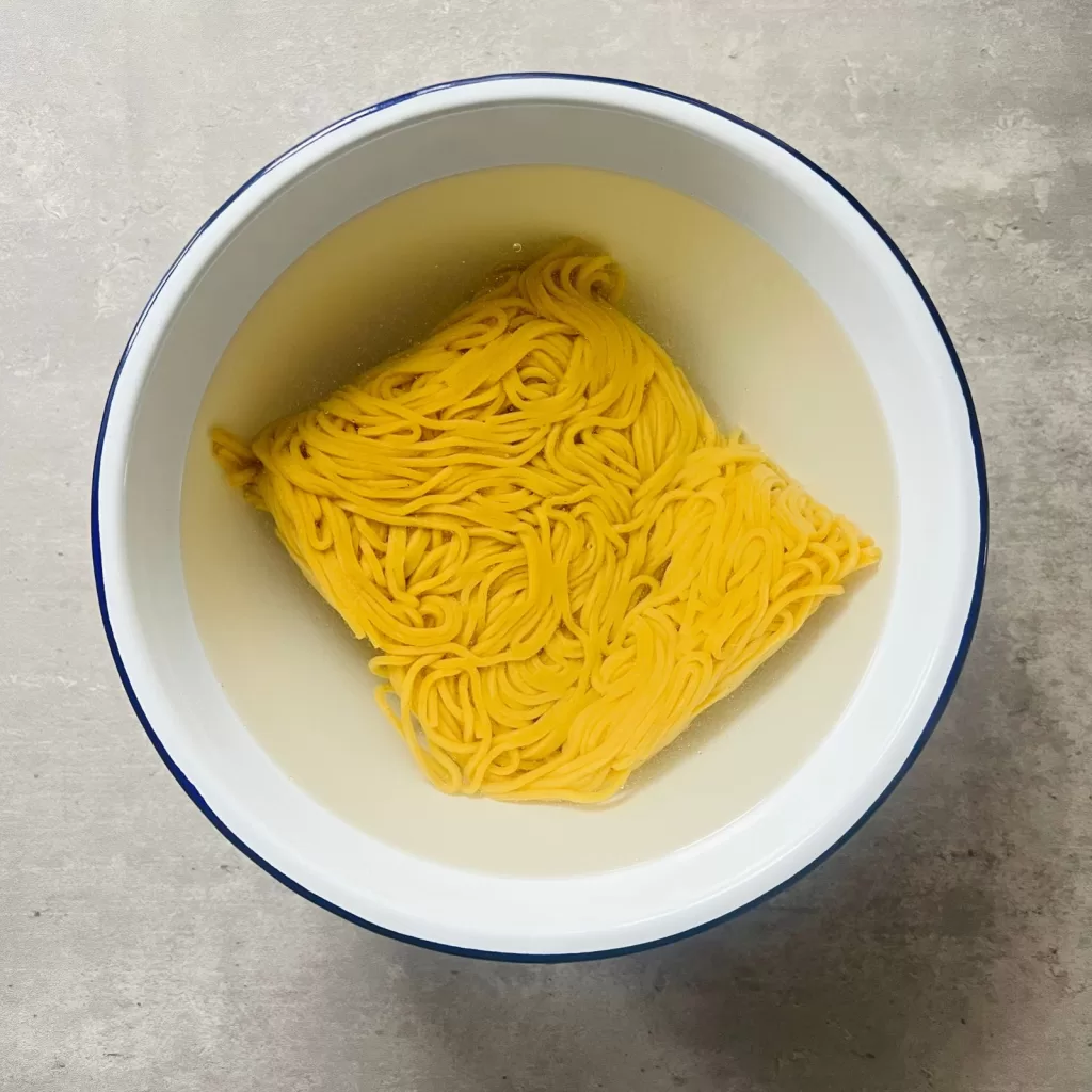 Hokkien noodles soaking in hot water to loosen before cooking satay chicken noodles.