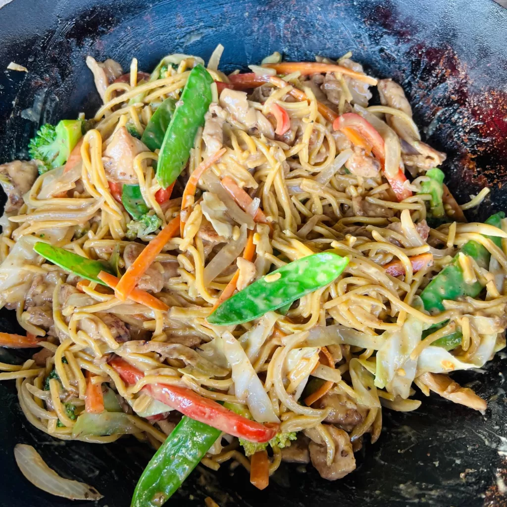 Satay chicken noodles tossed together in the wok until coated and glossy.