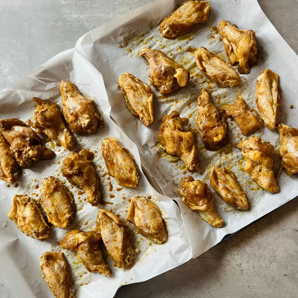 Raw chicken wings coated in satay marinade arranged on a lined baking tray before cooking