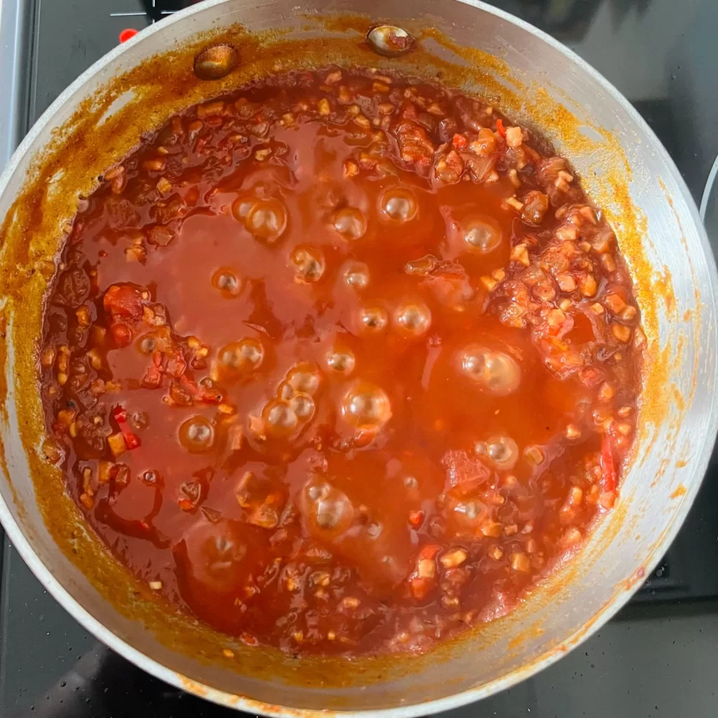Tomato bacon and chilli jam simmering in a saucepan until thick and glossy