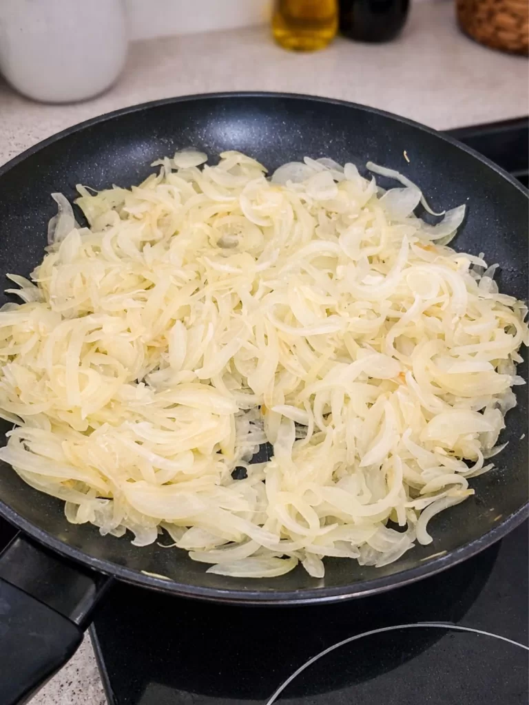 Sliced onions cooking in a non-stick frying pan, turning soft and translucent on a stovetop in natural light.