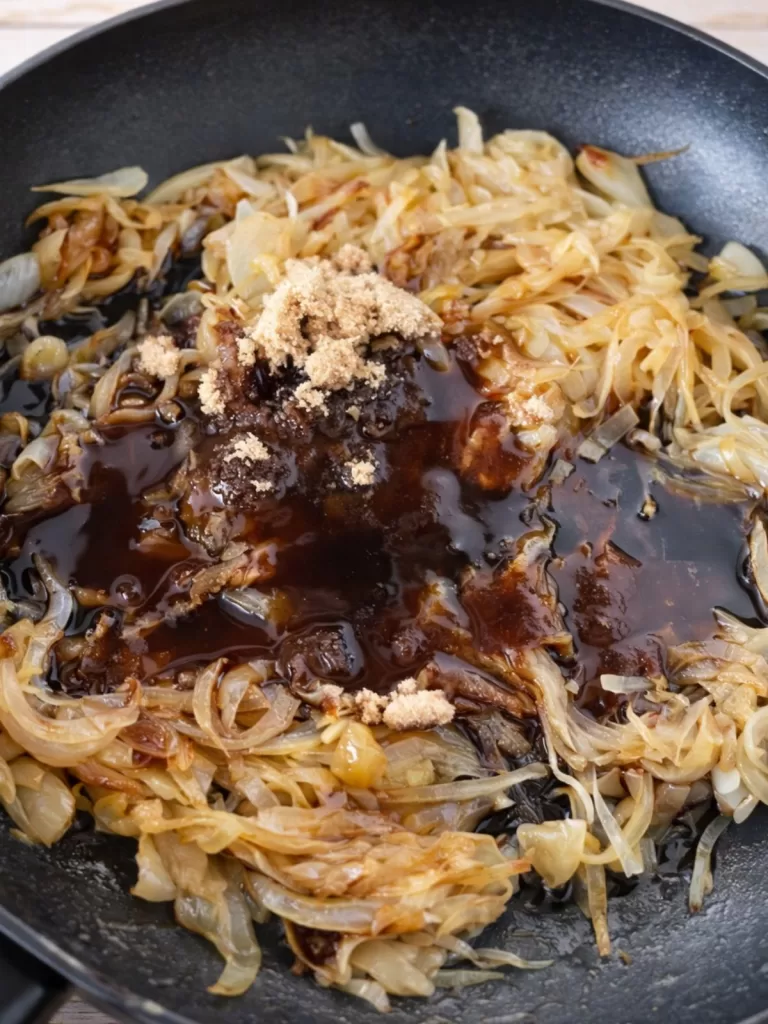 Caramelising onions in a frying pan with balsamic vinegar and brown sugar added, shown mid-cook in natural light.
