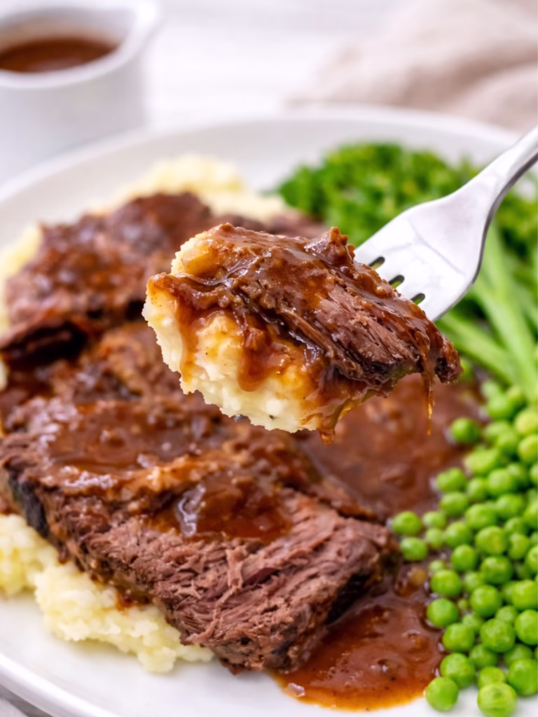 Close up of slow cooker beef bolar blade with gravy on mashed potatoes held on a fork