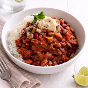 5 ingredient bean chilli with rice topped with sour cream and coriander in a white bowl on a light timber background