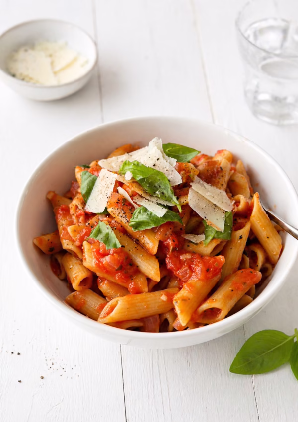 5 ingredient tomato pasta with penne, topped with parmesan and fresh basil in a white bowl