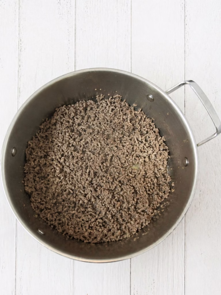browned beef mince in a saucepan on a white timber background