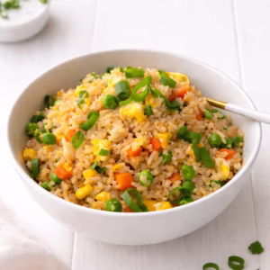 vegetable fried rice with frozen vegetables in a white bowl on a white timber surface, topped with sliced spring onions.