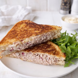 Tuna melt toastie cut in half on a white plate with rocket, showing a creamy tuna filling and golden toasted bread