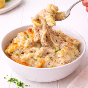 Creamy tuna pasta bake with melted cheese and parsley in a white bowl on a white timber background
