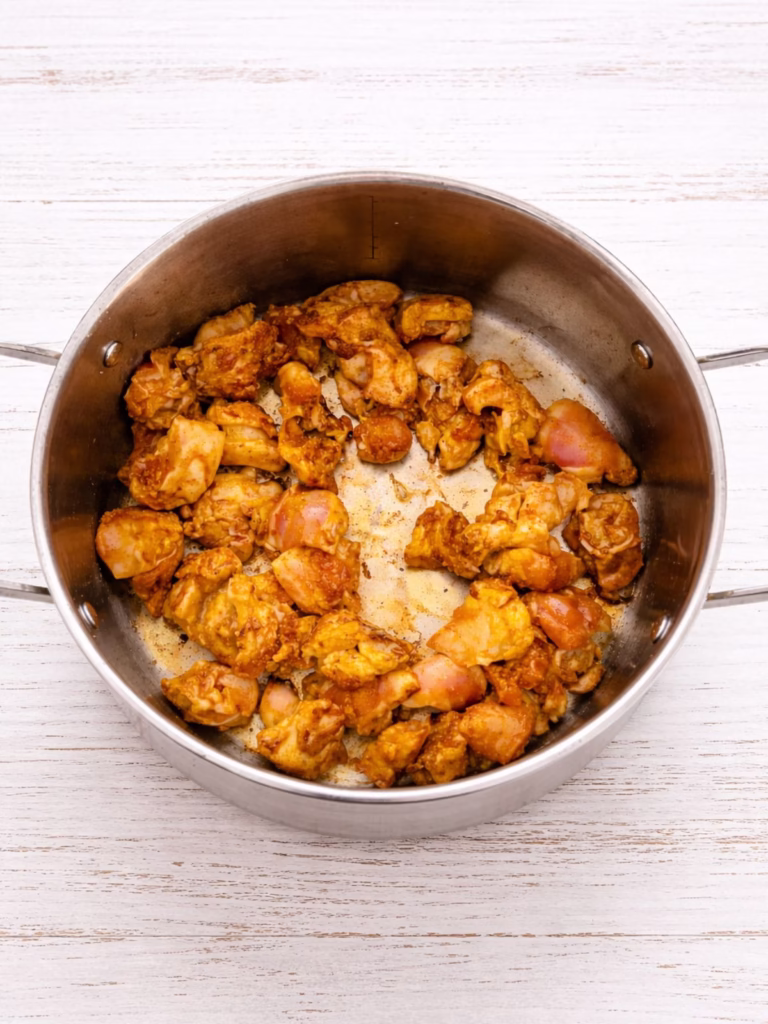 Golden chicken pieces cooking in a pan on a white timber background