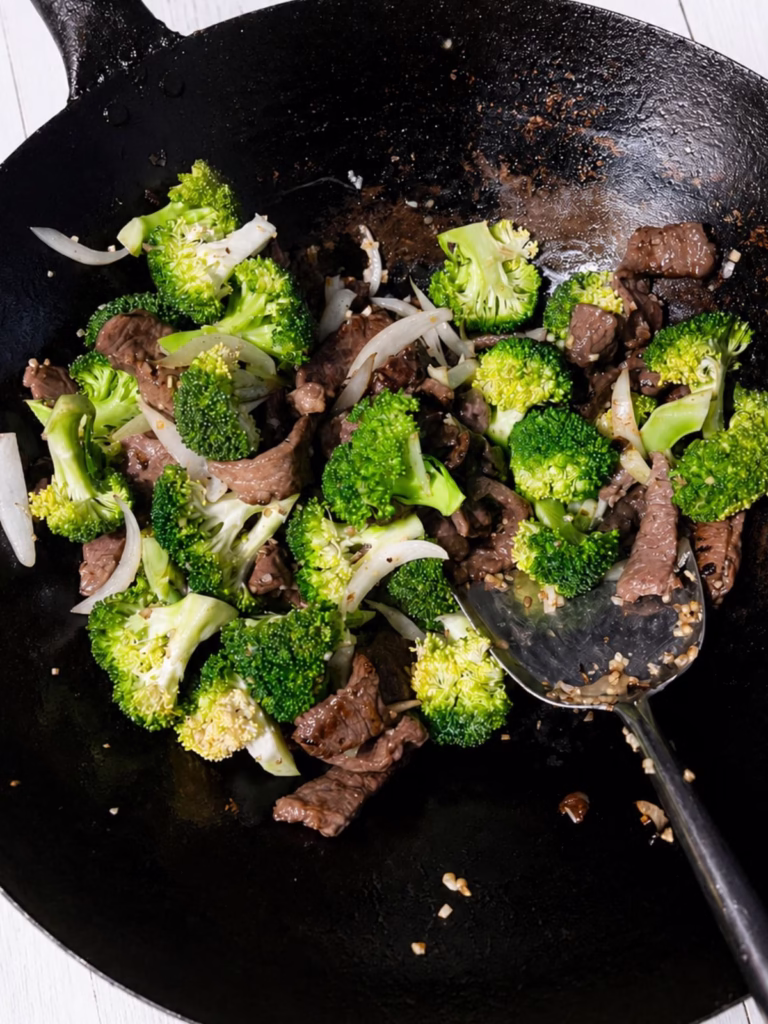 Beef and broccoli stir fry cooking in a black wok.