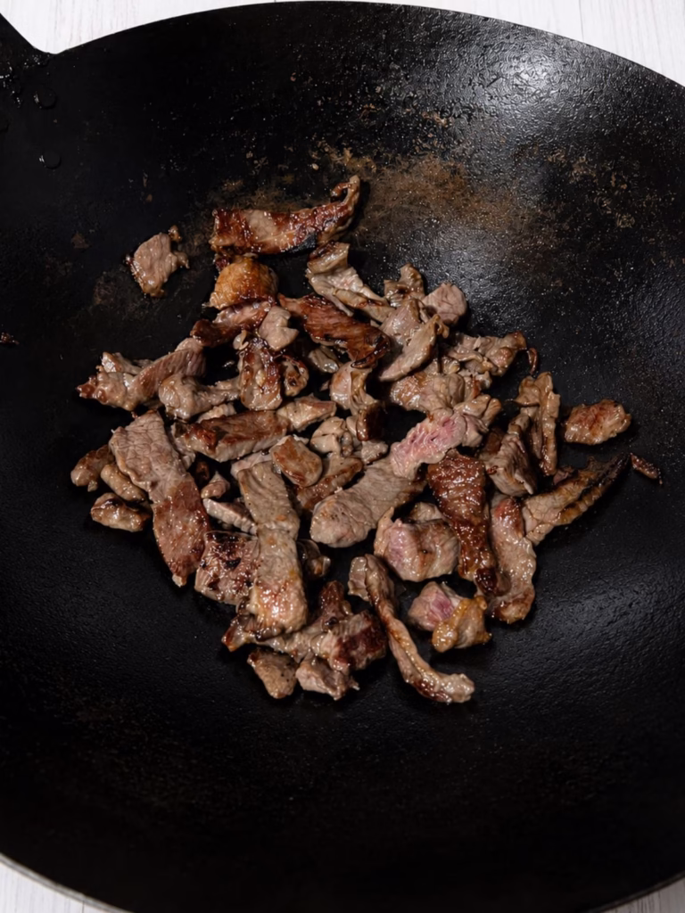 Close up image of browned sliced beef strips in a black wok.