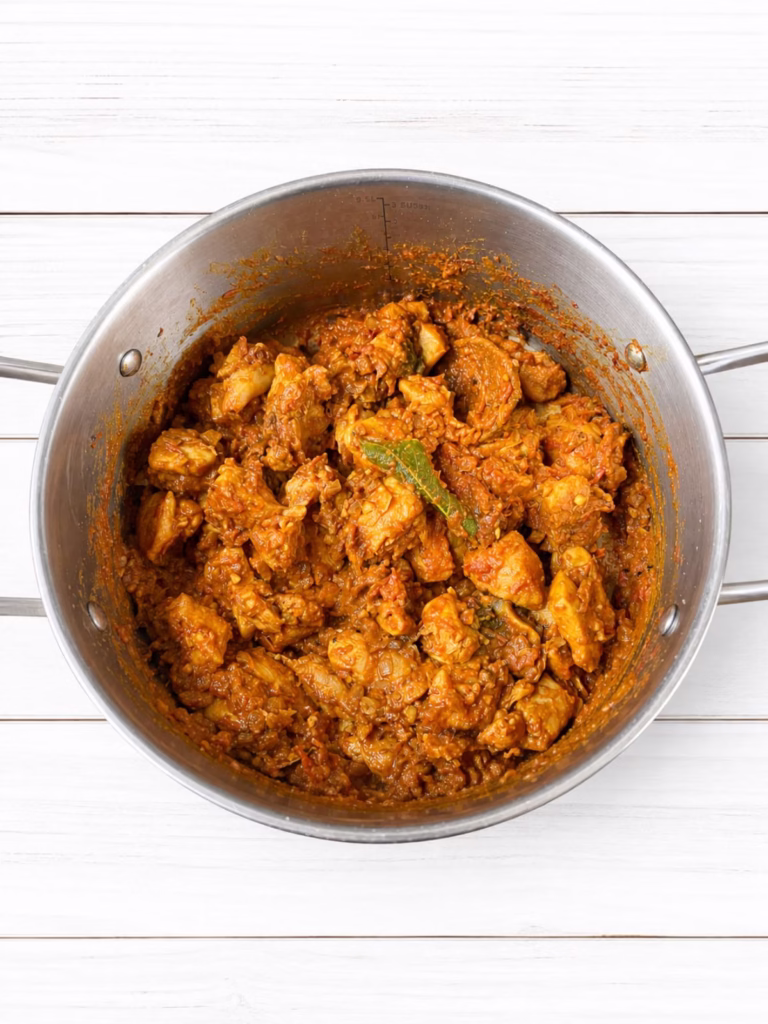 Tomato mixture simmering with softened onion and whole spices in a stainless steel saucepan