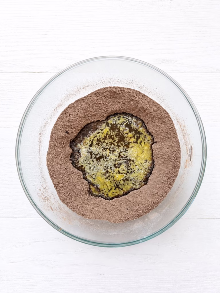 Melted butter and golden syrup added to cocoa and dry ingredients in a glass bowl ready to mix for chocolate caramel slice