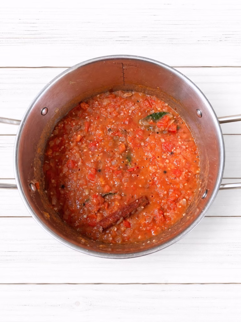 Tomato mixture simmering with softened onion and whole spices in a stainless steel saucepan